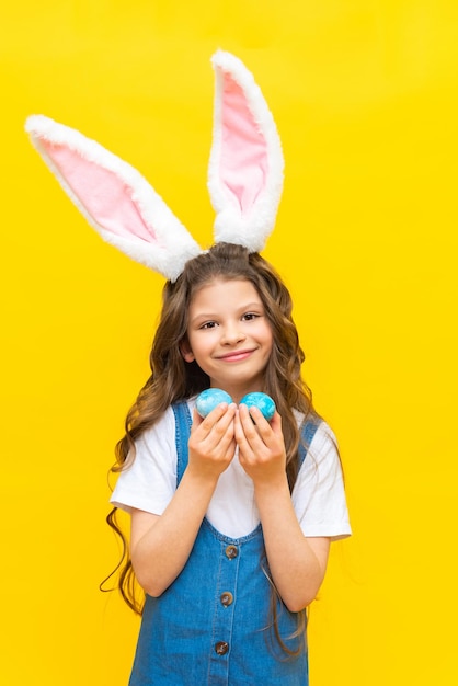 Buona Pasqua Una bambina tiene due uova dipinte per la vacanza Un bambino affascinante con orecchie di coniglio su uno sfondo giallo isolato