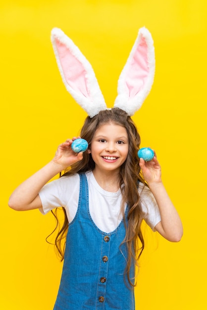 Buona Pasqua Una bambina tiene due uova dipinte per la vacanza Un bambino affascinante con orecchie di coniglio su uno sfondo giallo isolato