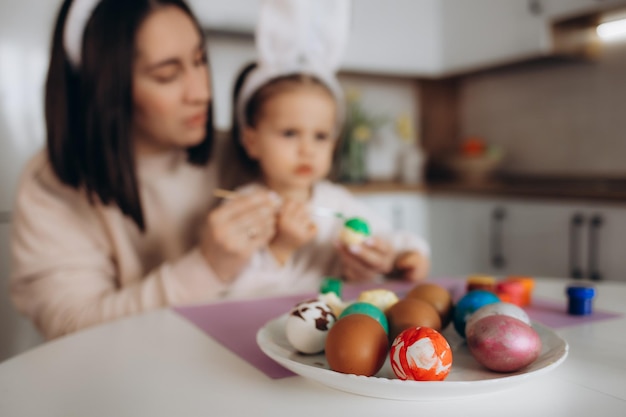 Buona Pasqua Una madre e sua figlia che dipingono le uova di Pasqua Famiglia felice che si prepara per la Pasqua Bambina carina che indossa orecchie da coniglio il giorno di Pasqua