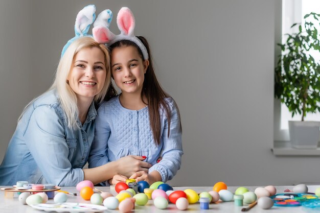 Buona Pasqua. Una madre e sua figlia dipingono le uova di Pasqua. Famiglia felice che si prepara per la Pasqua. Bambina sveglia che indossa le orecchie da coniglio il giorno di Pasqua.