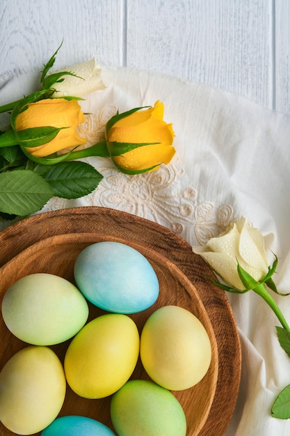 Buona Pasqua Uova di Pasqua su tavola rustica con rose bianche e gialle Uova colorate tinte naturali in piatto di legno e fiori primaverili in camera rustica Immagine tonica Sfondo di Pasqua con spazio di copia