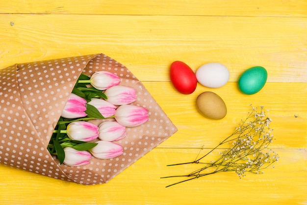 Buona stagione pasquale Raccolta delle uova di Pasqua Uova colorate e bouquet di fiori di tulipano freschi su sfondo giallo vista dall'alto Tradizione celebrare la Pasqua Saluti sinceri Vibrazioni pasquali Vacanze di primavera