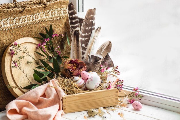 Buona tavola di Pasqua. Uova di Pasqua rosa in un nido con decorazioni floreali e piume vicino alla finestra