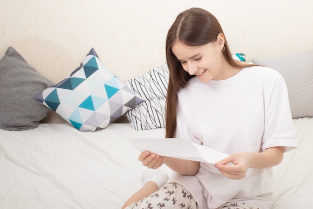 Buone notizie. La ragazza legge una lettera su un foglio di carta a casa, sorridente