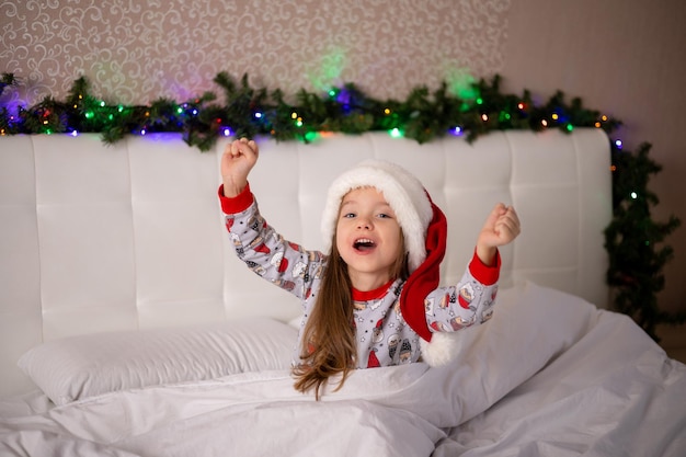 Buone vacanze e buon Natale Mattina Una ragazza allegra e divertente in pigiama e berretto da Babbo Natale