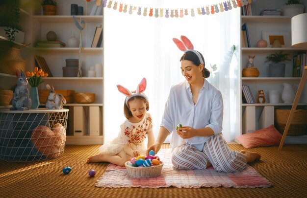 Buone vacanze Madre e figlia con uova di pittura Famiglia che celebra la Pasqua Cute bambina indossa orecchie da coniglio