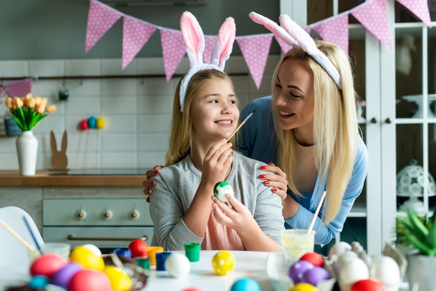 Buone vacanze! Una madre e sua figlia stanno dipingendo le uova. Famiglia che si prepara per la Pasqua. La bambina sveglia del bambino indossa le orecchie del coniglietto.