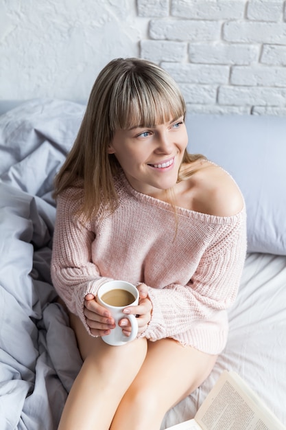 Buongiorno con il caffè. Giovane donna a letto con la tazza