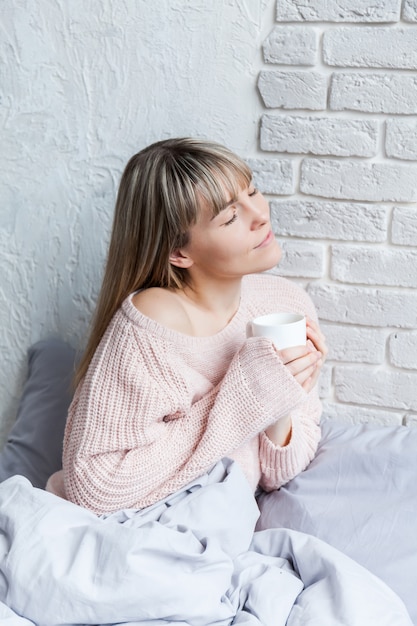 Buongiorno con il caffè. Giovane donna a letto con la tazza