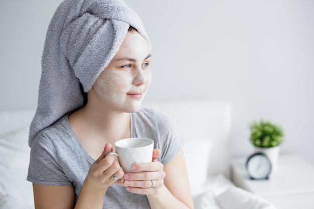 Buongiorno e concetto di cura della pelle Ritratto di giovane donna con maschera facciale in argilla che beve caffè