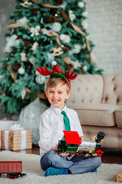 Buongiorno. Ragazzino felice con un regalo, trenino, sotto l'albero di Natale. È ora di soddisfare i desideri.