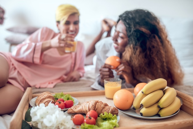 Buongiorno. Vassoio con colazione sana leggera e fiori e due amiche felici in vestiti da notte in sottofondo