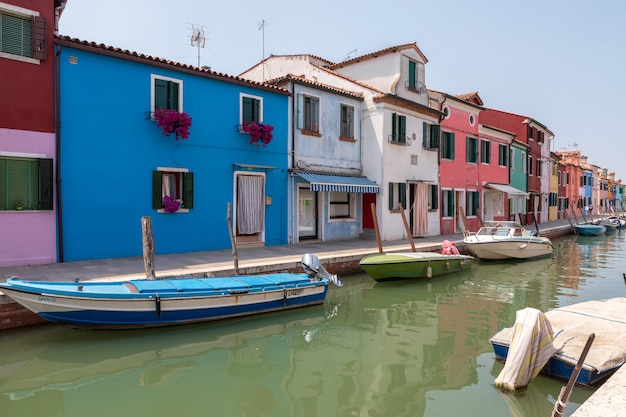 Burano, Venezia, Italia - 2 luglio 2018: Vista panoramica di case dai colori vivaci e canale d'acqua con barche a Burano, è un'isola della laguna veneziana. La gente cammina e riposa per strada