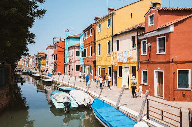 Burano, Venezia, Italia - 2 luglio 2018: Vista panoramica di case dai colori vivaci e canale d'acqua con barche a Burano, è un'isola della laguna veneziana. La gente cammina e riposa per strada