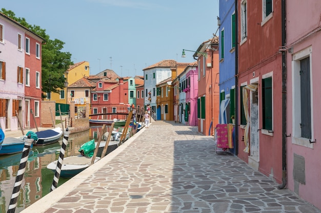 Burano, Venezia, Italia - 2 luglio 2018: Vista panoramica di case dai colori vivaci e canale d'acqua con barche a Burano, è un'isola della laguna veneziana. La gente cammina e riposa per strada