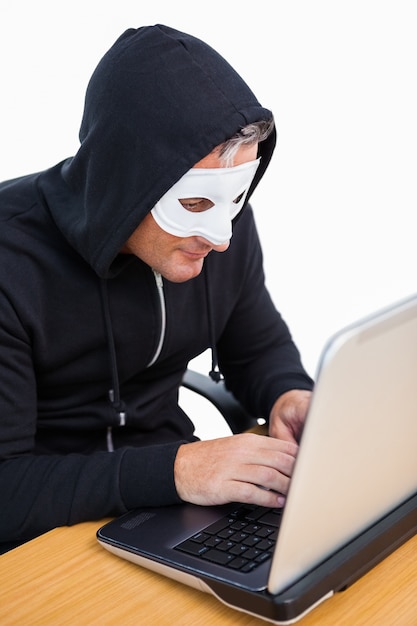 Burglar con la mascherina bianca che incide un computer portatile