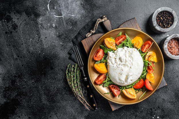 Burrata con pomodorini e rucola fresca in un piatto Sfondo nero Vista dall'alto Spazio di copia