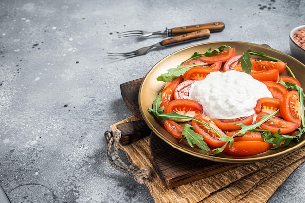 Burrata di stracciatella di formaggio italiano su piatto con pomodori freschi e rucola Sfondo grigio Vista dall'alto Spazio di copia