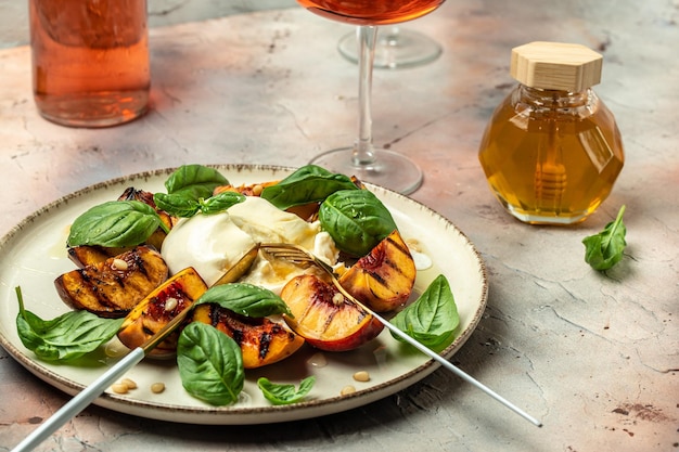 Burrata e pesche grigliate con basilico e pinoli Due bicchieri di vino rosato su sfondo chiaro Delizioso antipasto posto per testo vista dall'alto