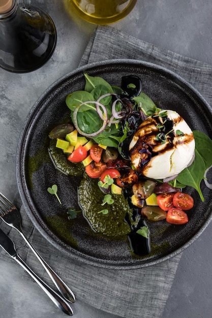 Burrata formaggio fresco italiano con salsa al pesto e verdure. Bottiglie con salsa, tovaglia grigia, cucchiaio e forchetta. Di fronte alla grande finestra del ristorante. Vista dall'alto