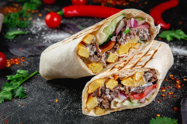 Burrito Shawarma tagliato con verdure ed erbe aromatiche su un tavolo di pietra scuro Il concetto di fast food