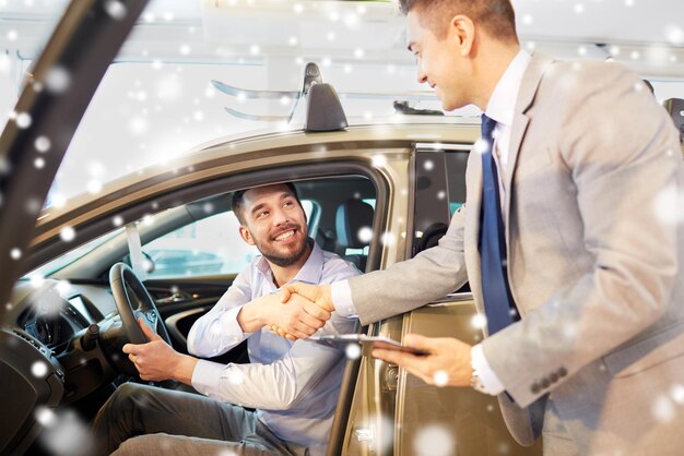 business automobilistico, vendita di auto, consumismo, gesto e concetto di persone - uomo felice con un rivenditore di auto che fa affari e stringe la mano in auto show o salone sopra l'effetto neve