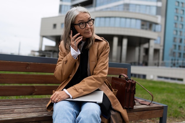 Business donna d'affari anziana parlando su un telefono cellulare con un laptop in grembo contro il