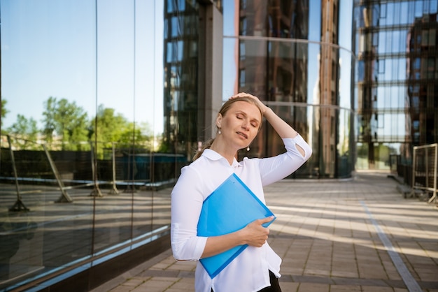 Business donna di successo in camicia bianca con cartella blu per documenti si trova in edificio per uffici