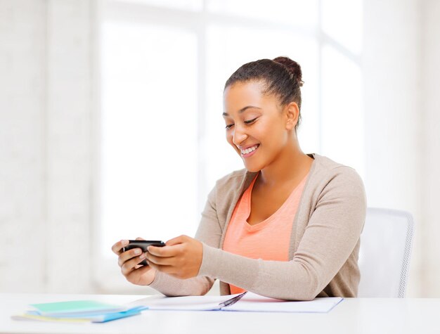 business e concetto di comunicazione - donna africana sorridente con lo smartphone in ufficio