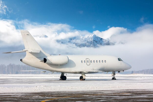 Business jet bianco sul piazzale invernale dell'aeroporto sullo sfondo di alte montagne panoramiche