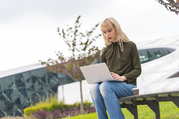 Business park biondo caucasico dell'imprenditore della ragazza che invia un'e-mail con il computer portatile. Poligono moderno in mezzo alla natura