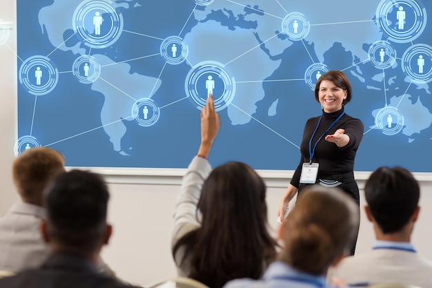 business, rete globale e concetto di persone - donna d'affari o docente sorridente con una mappa del mondo sullo schermo di proiezione che risponde alle domande durante la presentazione o la conferenza di una conferenza