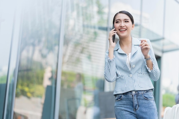 business tecnologia comunicazione idee concetto intelligente attraente donna asiatica camicia casual sorridere e godere di conversazione con smartphone gesto della mano con sfondo del moderno negozio vetrina anteriore display