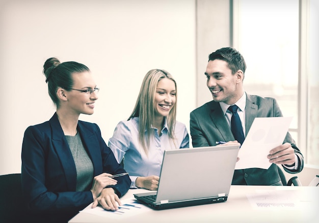Business, tecnologia e concetto di ufficio - sorridente business team con computer portatili e documenti che hanno discussione in ufficio