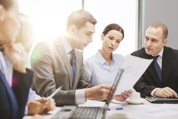 business, tecnologia e concetto di ufficio - team di lavoro serio con computer portatili, documenti e caffè che discutono in ufficio