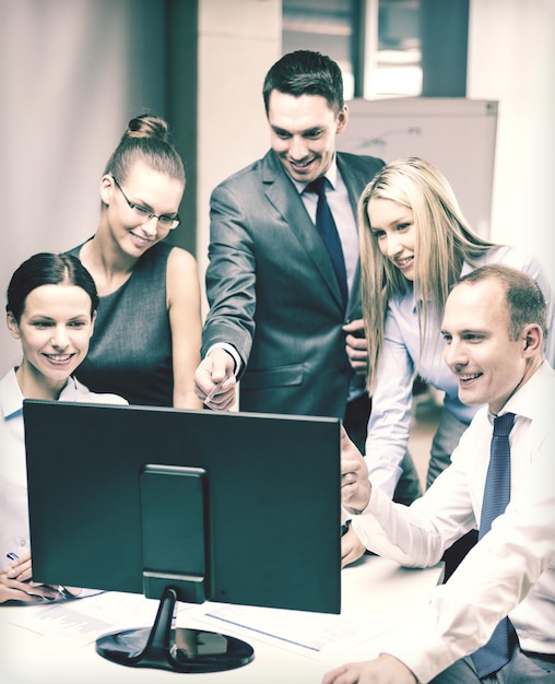 business, tecnologia e concetto di ufficio - team di lavoro sorridente con monitor di computer che discute in ufficio