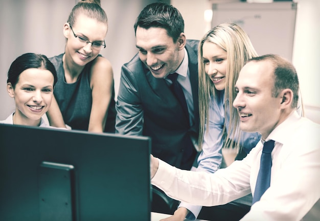 business, tecnologia e concetto di ufficio - team di lavoro sorridente con monitor di computer che discute in ufficio