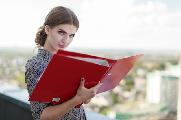 Businesslady attraente in abito fantasia stare sul tetto e tenere la cartella di carta