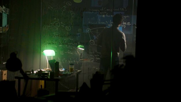 businessman writing notes on the glass board near the mess on his table at night stock man