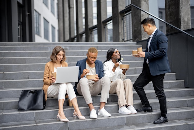 Businessteam multirazziale che parla di mangiare e bere caffè seduti sulle scale in città