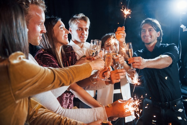 Bussare agli occhiali. Gruppo di amici allegri che festeggiano il nuovo anno in casa con un drink in mano.