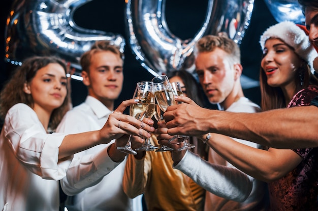 Bussare agli occhiali. Gruppo di amici allegri che festeggiano il nuovo anno in casa con un drink in mano.