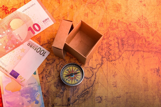 Bussola accanto a una scatola e banconote in euro su una vecchia mappa