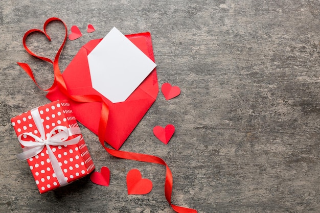 Busta di carta rossa con carta bianca vuota e cuore su sfondo colorato vista dall'alto concetto di giorno di san valentino