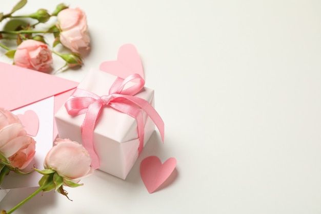 Busta, rose, cuori e confezione regalo su sfondo bianco