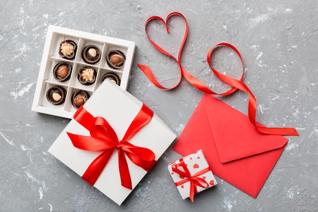 Busta su sfondo colorato per San Valentino con confezione regalo e cioccolato A forma di cuore con confezione regalo di cioccolatini vista dall'alto con spazio per la copia