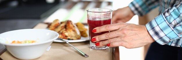 C'è insalata sul vassoio e la mano di una donna del secondo piatto tiene un bicchiere con un liquido rosso.