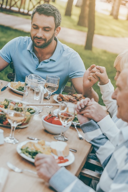 C'è sempre qualcosa di cui essere grati. Famiglia che si tiene per mano e prega prima di cena seduti a tavola all'aperto