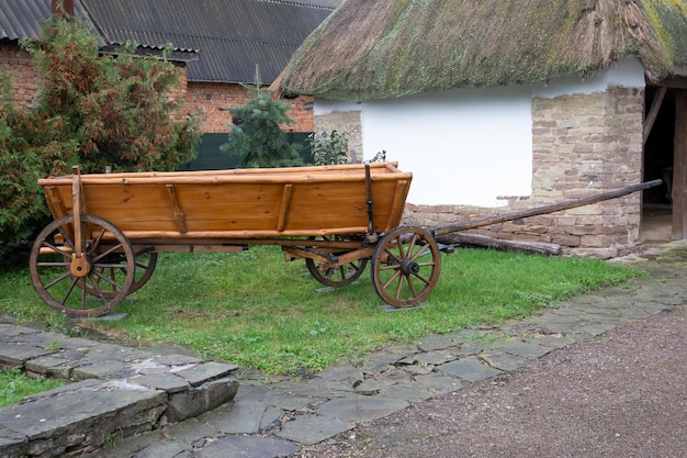 C'è un vecchio carro nel cortile. Su erba verde. Vicino alla vecchia casa.