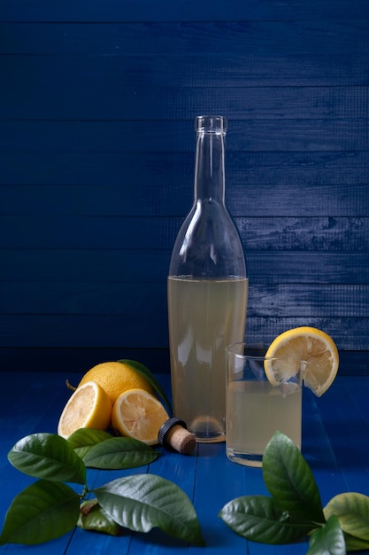 C'è una bottiglia di succo di limone e limoni sul tavolo. C'è un bicchiere nelle vicinanze.